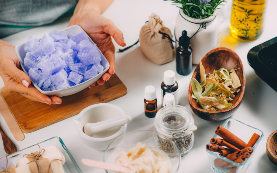 Assorted handmade soaps with natural ingredients like oils, botanicals, and colorants, displayed on a wooden surface.