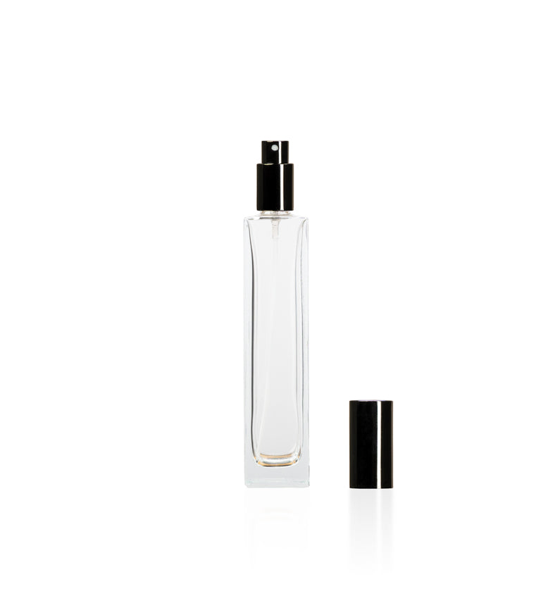Image of a tall, narrow, clear glass bottle with a black top on a white background to represent Village Craft & Candle's 4oz Charisma Bottle for room sprays. || Image d'une bouteille en verre claire, haute et étroite avec un bouchon noir sur un fond blanc pour représenter la bouteille Charisma de 4oz de Village Craft & Candle pour les vaporisateurs d'ambiance.