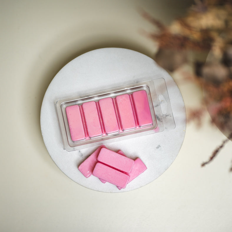 Image of pink wax melts in long snap bar clamshell on decorative dish on table to represent Village Craft & candle's Snap Bar clamshell mold for candle making and crafting. || Image de fondants de cire roses dans un moule long Snap Bar sur un plat décoratif sur une table, représentant le moule Snap Bar de Village Craft & Candle pour la fabrication de bougies et l'artisanat.