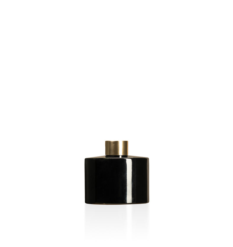 Image of a stout black glass diffuser bottle with a gold collar on a white background to represent Village Craft & Candle's Lavish Diffuser Bottle. || Image d'une bouteille de diffuseur en verre noire trapue avec un col doré sur un fond blanc pour représenter la bouteille de diffuseur Lavish de Village Craft & Candle.