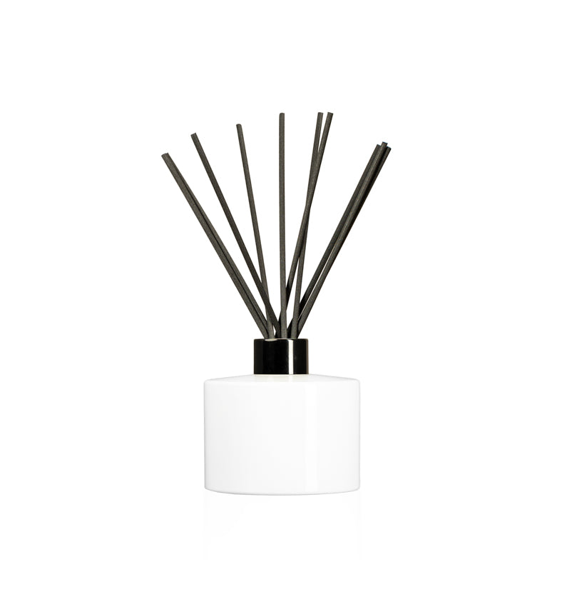 Image of a stout white glass diffuser bottle with a black collar & fiber reeds on a white background to represent Village Craft & Candle's Lavish Diffuser Bottle. || Image d'une bouteille de diffuseur en verre blanc trapue avec un col noir et des tiges en fibre sur fond blanc pour représenter la bouteille de diffuseur Lavish de Village Craft & Candle.
