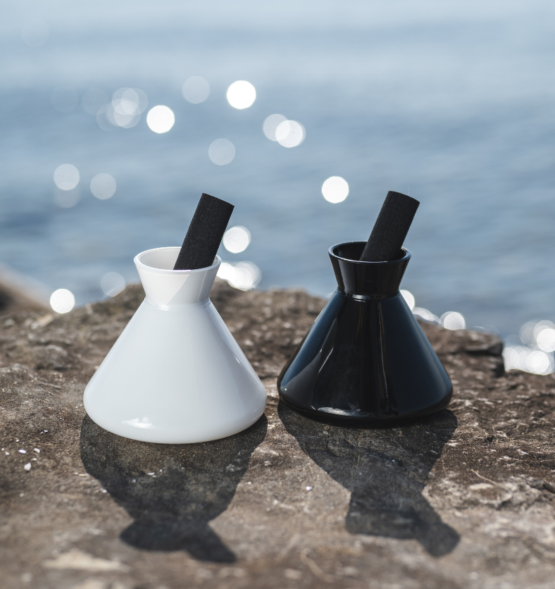 Image of black and white diffusers with black reed to represent Village Craft & Candle's Allure 9oz Diffusers from the Aromatics Collection. Diffusers are on a rock with a lake in the background. || Image de diffuseurs noir et blanc avec des tiges noires pour représenter les diffuseurs Allure 9 oz de Village Craft & Candle de la Collection Aromatics. Les diffuseurs sont posés sur un rocher avec un lac en arrière-plan.