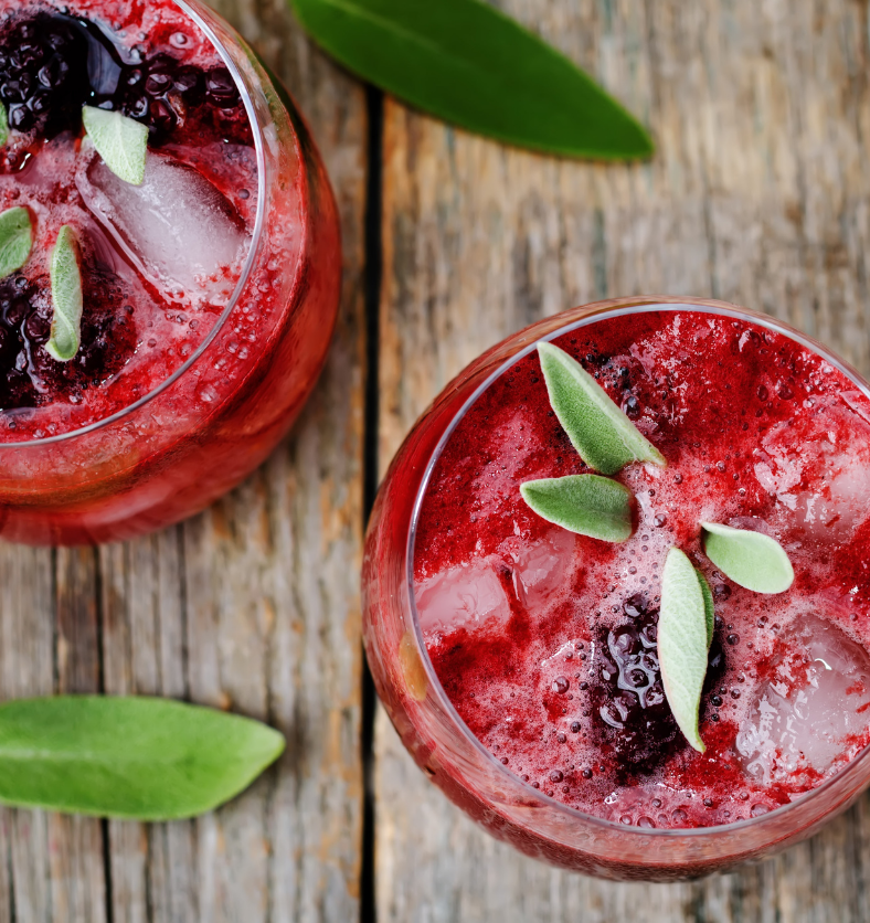 Birds eye view of red frothy drink with blackberry & sage garnish as a visual representation of Blackberry Sage Fragrance Oil available at Village Craft and Candle || Vue à vol d'oiseau d'une boisson mousseuse rouge avec une garniture de mûre et de sauge comme représentation visuelle de l'huile parfumée de mûre et de sauge disponible chez Village Craft and Candle