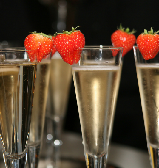 Flûtes Campange avec des fraises sur les lèvres des verres comme représentation visuelle de l'huile parfumée aux fraises et au champagne disponible chez Village Craft and Candle