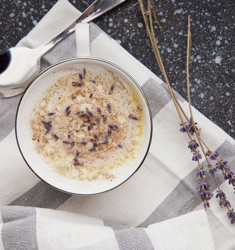 Top view of a cup of white hot cocoa with a lavender sprig as a visual representation of Cocoa & Lavender Fragrance Oil available at Village Craft and Candle || Vue de dessus d'une tasse de chocolat chaud blanc avec un brin de lavande comme représentation visuelle de l'huile parfumée de cacao et de lavande disponible chez Village Craft and Candle