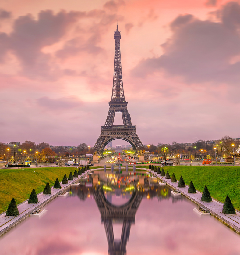 View of Eiffel Tower with pink skies and reflection in water as a visual representation of Evening Mischief Fragrance Oil available at Village Craft and Candle || Vue de la Tour Eiffel avec un ciel rose et son reflet dans l'eau comme représentation visuelle de l'huile parfumée Evening Mischief disponible chez Village Craft and Candle.