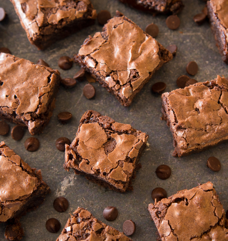 Brownie squares with chocolate chips surrounding them as a visual representation of Hot Fudge Brownie Fragrance Oil available at Village Craft and Candle || Carrés de brownie entourés de pépites de chocolat comme représentation visuelle de l'huile parfumée Hot Fudge Brownie disponible chez Village Craft and Candle.
