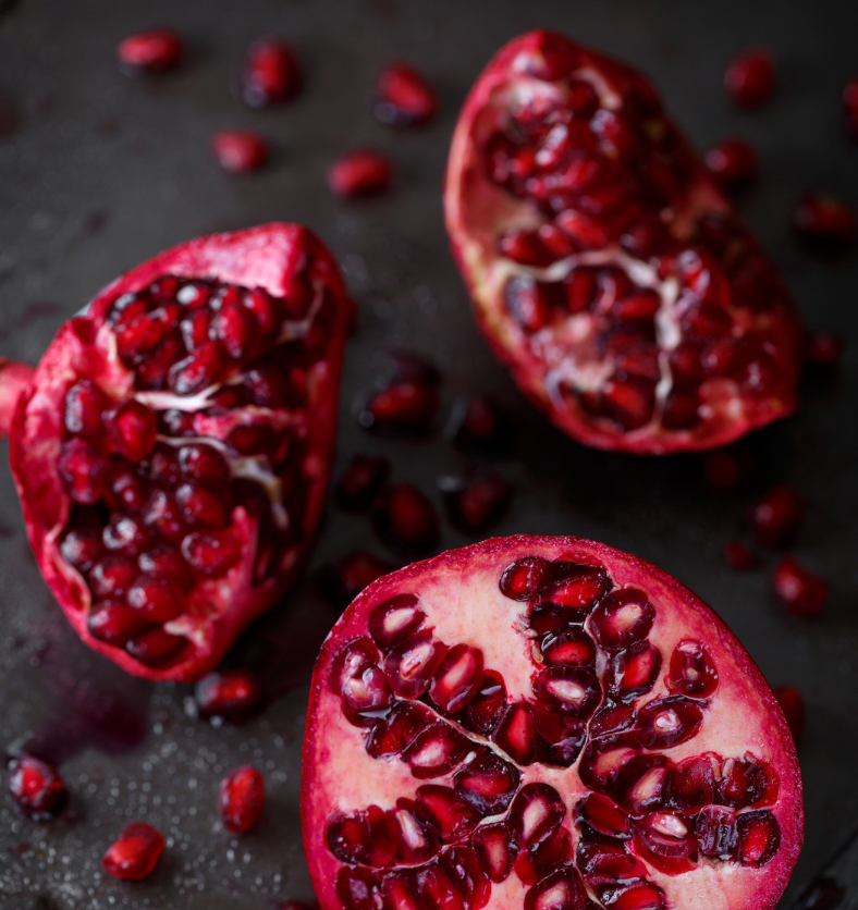 Crushed pomegranates on a black countertop as a visual representation of Jeweled Pomegranate Fragrance Oil available at Village Craft and Candle || Grenades écrasées sur un comptoir noir comme représentation visuelle de l'huile parfumée Jeweled Pomegranate disponible chez Village Craft and Candle