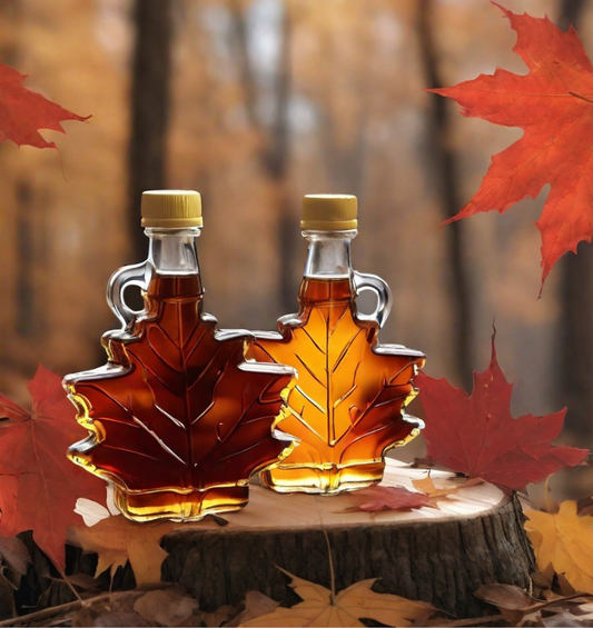 Two bottle of maple syrup in maple leaf shaped bottles on tree stump surrounded by red maple leaves as a visual representation of Maple Syrup Fragrance Oil available at Village Craft and Candle