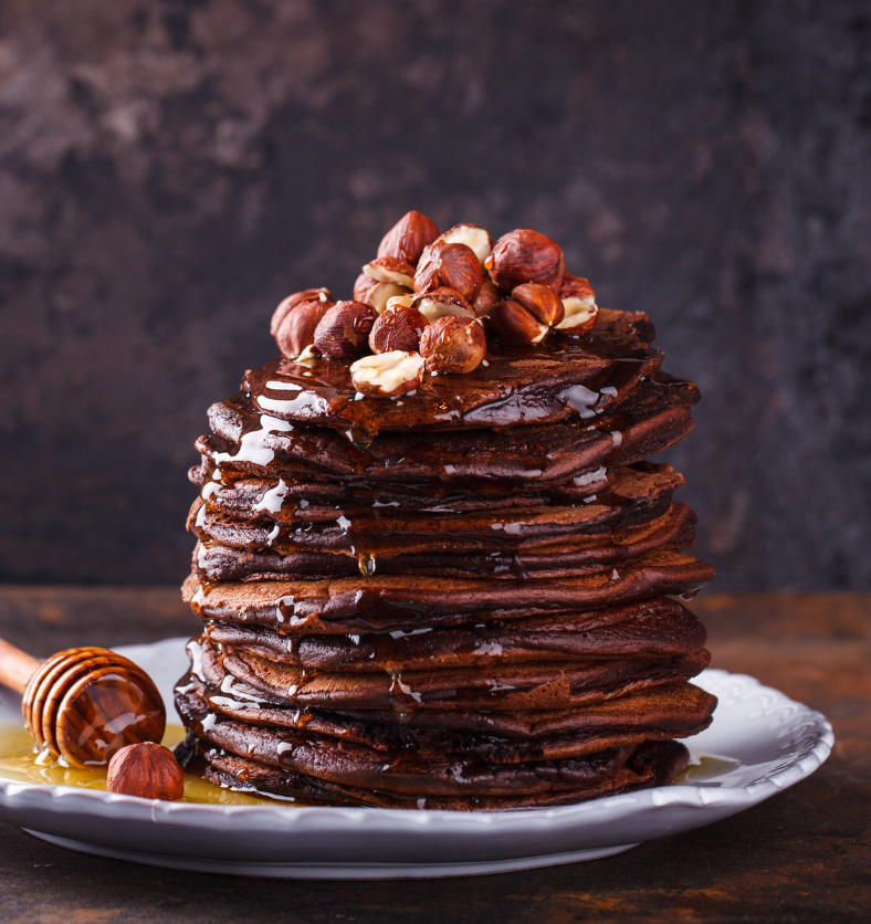 Stack of crepes and pancakes drizzled in honey and chocolate as a visual representation of Maple Syrup & Hazelnut Fragrance Oil available at Village Craft and Candle || Pile de crêpes et de crêpes arrosées de miel et de chocolat comme représentation visuelle de l'huile parfumée au sirop d'érable et aux noisettes disponible chez Village Craft and Candle