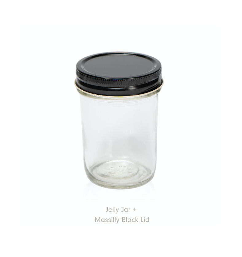 A clear jelly jar with a black Massilly lid on a white background. || Un pot à confiture transparent avec un couvercle noir Massilly sur fond blanc.