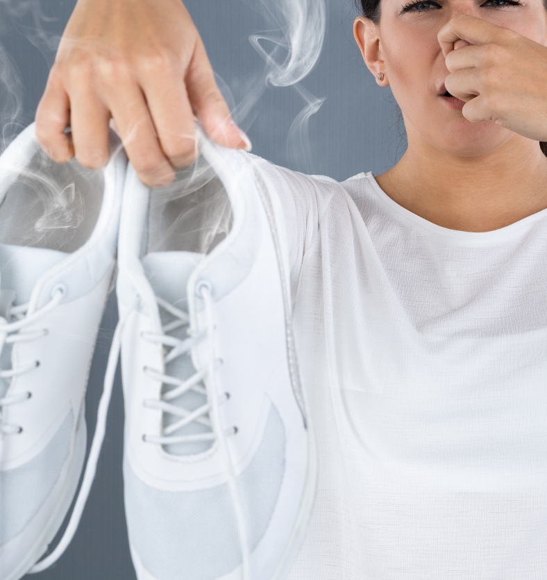 Woman holding stinky white tennis shoes as a visual representation of Odor Eater Fragrance Oil available at Village Craft and Candle || Womand tenant des chaussures de tennis blanches puantes comme représentation visuelle de l'huile parfumée Odor Eater disponible chez Village Craft and Candle