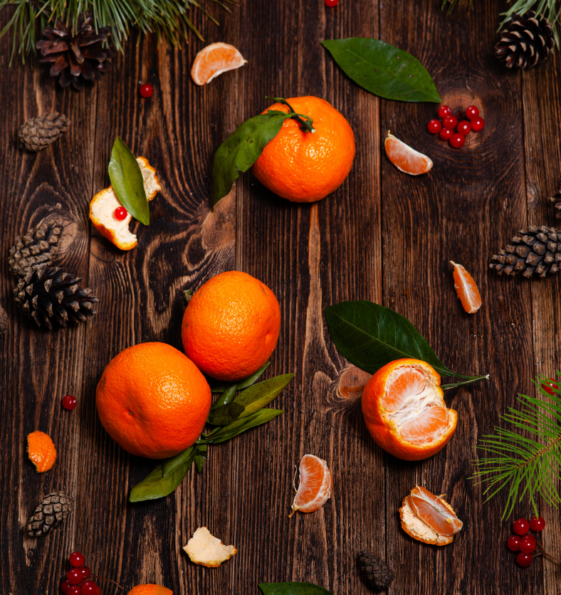 Oranges and pinecones on a wood table as a visual representation of Oriental Christmas Fragrance Oil available at Village Craft and Candle || Oranges et pommes de pin sur une table en bois comme représentation visuelle de l'huile parfumée de Noël orientale disponible chez Village Craft and Candle