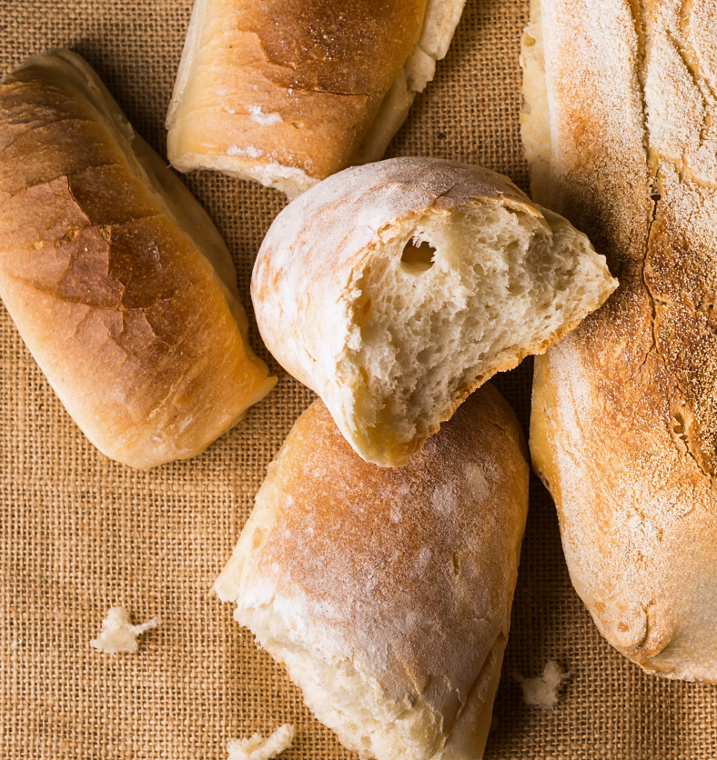 Broken baguettes on a burlap tablecloth as a visual representation of Oven Fresh Bread Fragrance Oil available at Village Craft and Candle || Baguettes cassées sur une nappe en toile de jute comme représentation visuelle de l'huile parfumée de pain frais au four disponible chez Village Craft and Candle