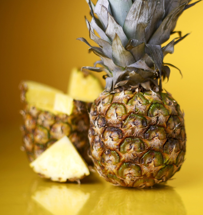 Pineapple slices with a full pineapple in the background as a visual representation of Pineapple Fragrance Oil available at Village Craft and Candle || Tranches d'ananas avec un ananas entier en arrière-plan comme représentation visuelle de l'huile parfumée d'ananas disponible chez Village Craft and Candle.