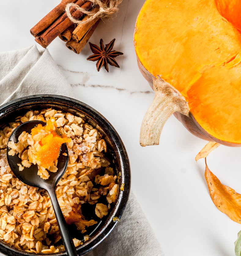 Cut pumpkin, cinnamon, cloves, and oats on a white marble background as a visual representation of Pumpkin Crumble Fragrance Oil available at Village Craft and Candle || Coupez la citrouille, la cannelle, les clous de girofle et l'avoine sur un fond de marbre blanc comme représentation visuelle de l'huile parfumée Pumpkin Crumble disponible chez Village Craft and Candle.