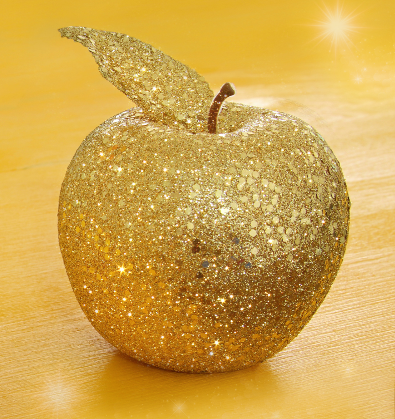 Golden encrusted apple on a yellow oak table as a visual representation of Razzle Dazzle Apple Fragrance Oil available at Village Craft and Candle || Pomme incrustée d'or sur une table en chêne jaune comme représentation visuelle de l'huile parfumée de pomme Razzle Dazzle disponible chez Village Craft and Candle