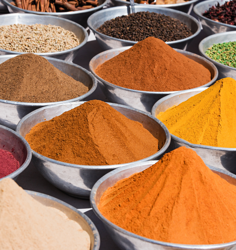 Stainless steel bowls of various colourful spices in a market as a visual representation of Rooibos Saffron Fragrance Oil available at Village Craft and Candle || Vieux barils de diverses épices colorées sur un marché comme représentation visuelle de l'huile parfumée Rooibos Safran disponible chez Village Craft and Candle