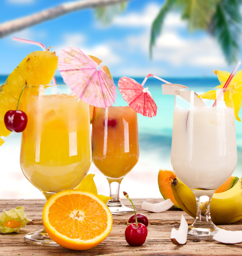 Tropical drinks with fruits and paper umbrellas on a beach as a visual representation of Sex on the Beach Fragrance Oil available at Village Craft and Candle || Boissons tropicales avec fruits et parasols en papier sur une plage comme représentation visuelle de l'huile parfumée Sex on the Beach disponible chez Village Craft and Candle