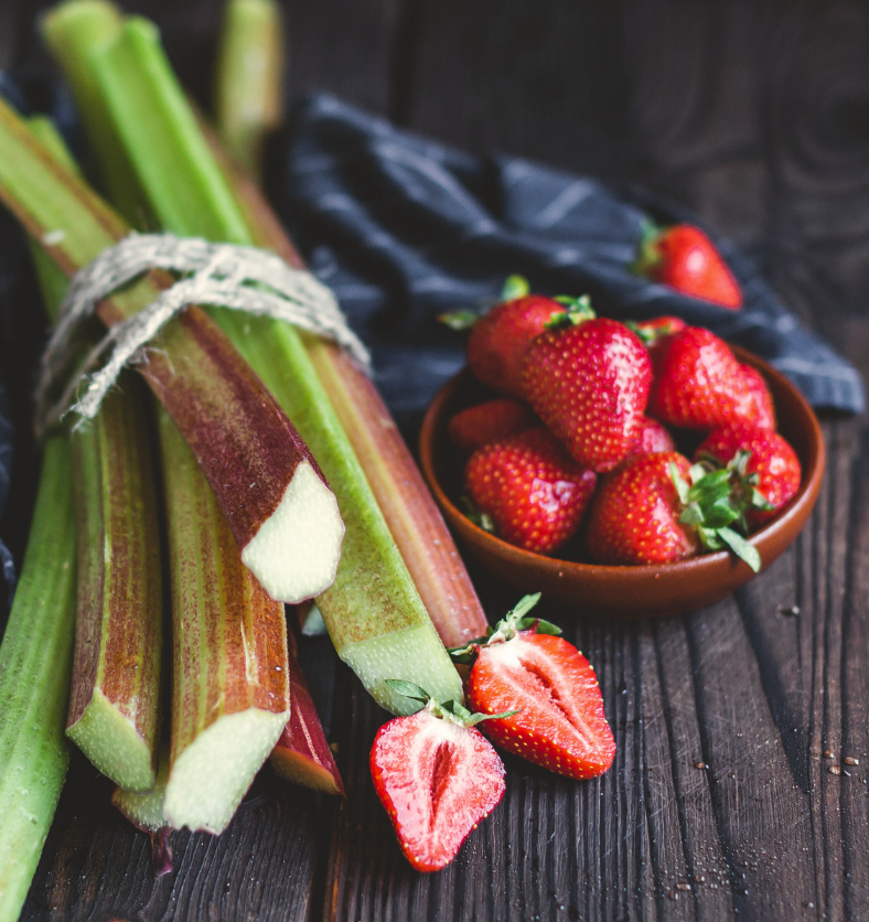 Bowl of strawberries & a bundle of fresh rhubarb as a visual representation of Rhubarb Strawberry Fragrance Oil available at Village Craft and Candle || Bol de fraises et un paquet de rhubarbe fraîche comme représentation visuelle de l'huile parfumée à la rhubarbe et à la fraise disponible chez Village Craft and Candle
