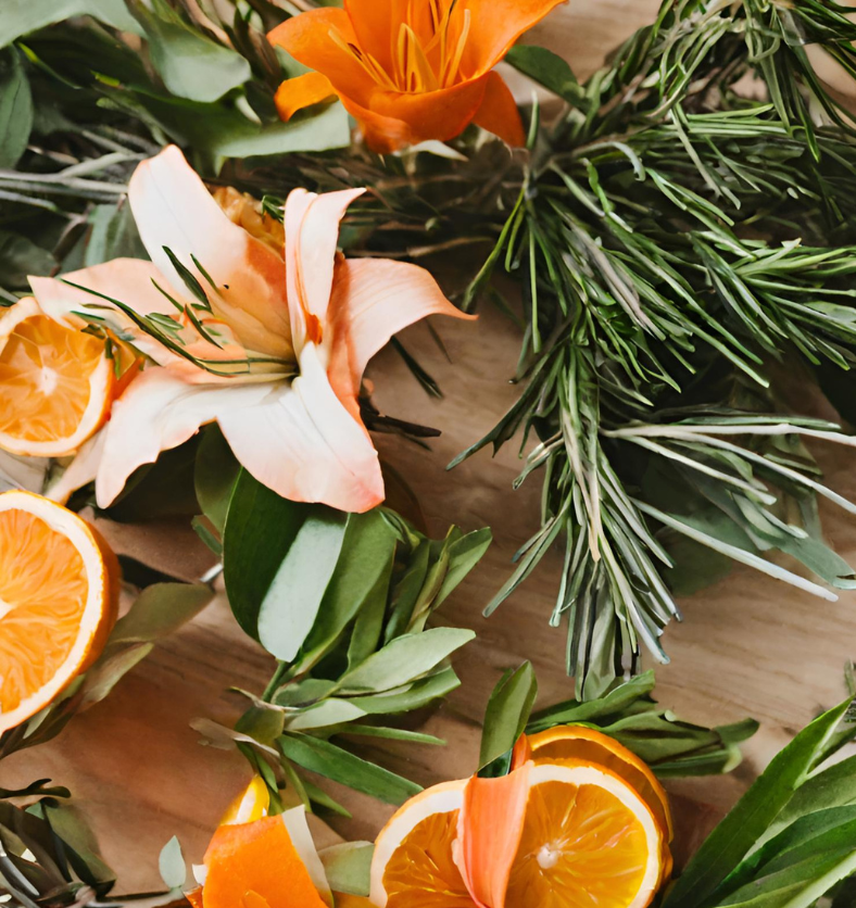 Image of fir needles, sliced oranges & rosemary on a wood table to represent Village Craft & Candle's Timberlake Fragrance Oil. || Image d'aiguilles de sapin, d'oranges tranchées et de romarin sur une table en bois pour représenter l'huile parfumée Timberlake de Village Craft & Candle.