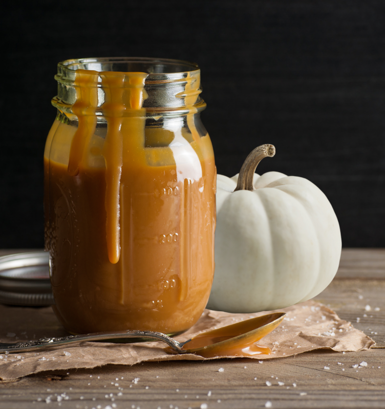 Mason jar of caramel next to a white pumpkin as a visual representation of White Pumpkin & Caramel Fragrance Oil available at Village Craft and Candle || Pot Mason de caramel à côté d'une citrouille blanche comme représentation visuelle de l'huile parfumée de citrouille blanche et de caramel disponible chez Village Craft and Candle