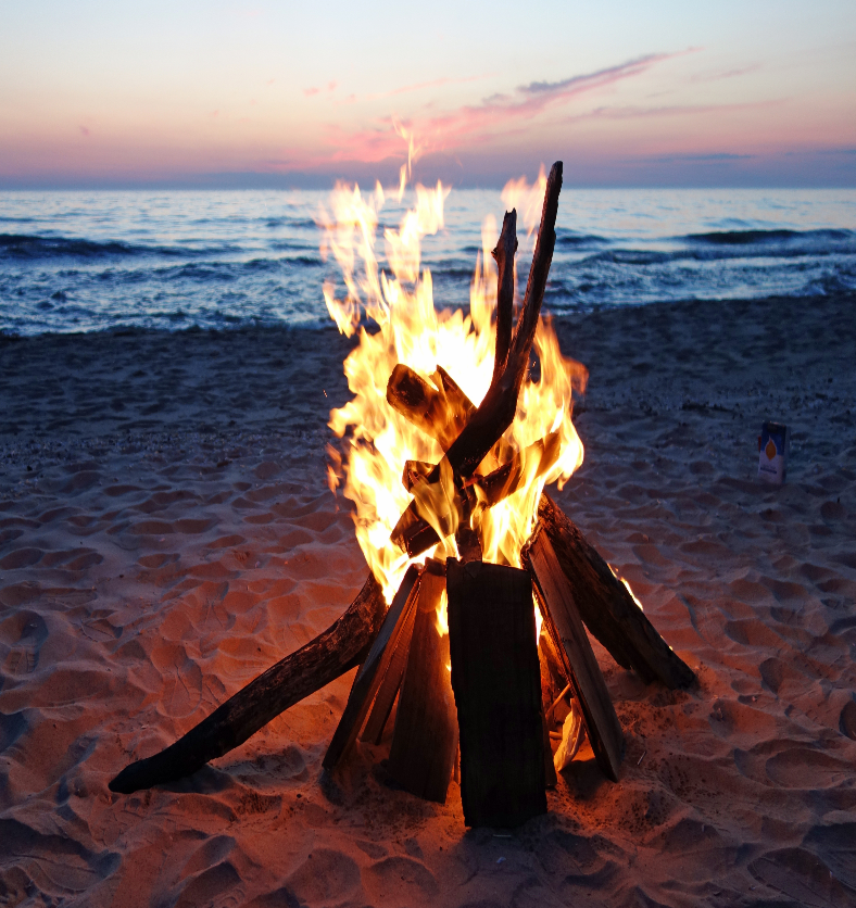 Campfire burning on a beach at sunset as a visual representation of Campfire Fragrance Oil available at Village Craft and Candle || Feu de camp brûlant sur une plage au coucher du soleil comme représentation visuelle de l'huile parfumée de feu de camp disponible chez Village Craft and Candle