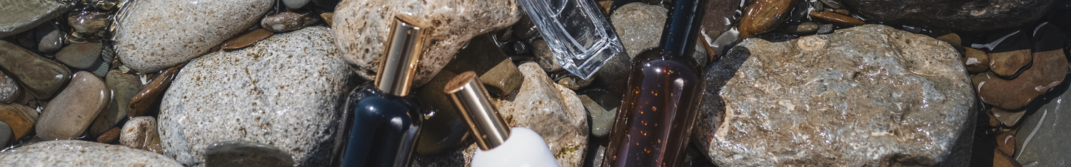 black, white, amber and clear room sprays with gold or black lids in water amongst pebbles