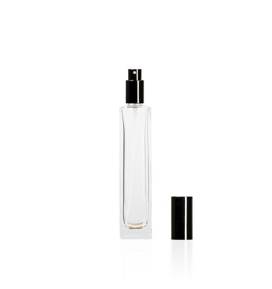 Image of a tall, narrow, clear glass bottle with a black top on a white background to represent Village Craft & Candle's 4oz Charisma Bottle for room sprays. 
