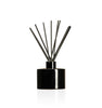 Image of a stout black glass diffuser bottle with a black collar & fiber reeds on a white background to represent Village Craft & Candle's Lavish Diffuser Bottle. || Image d'une bouteille de diffuseur en verre noire trapue avec un col noir et des tiges en fibre sur un fond blanc pour représenter la bouteille de diffuseur Lavish de Village Craft & Candle.