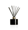 Image of a stout black glass diffuser bottle with a gold collar & fiber reeds on a white background to represent Village Craft & Candle's Lavish Diffuser Bottle. || Image d'une bouteille de diffuseur en verre noire trapue avec un col doré et des tiges en fibre sur un fond blanc pour représenter la bouteille de diffuseur Lavish de Village Craft & Candle.