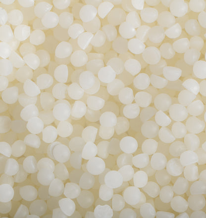 Close up image of white beads of wax to represent Village Craft & Candles White Beeswax Pastilles. || Gros plan d'une image de perles de cire blanche pour représenter les pastilles de cire blanche de Village Craft & Candles.