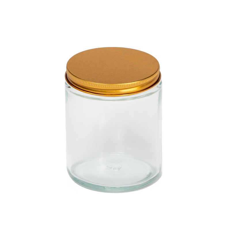 Image of a clear glass jar with a low profile gold lid to represent Village Craft & Candle's 8oz Clear Flint Element Straight Side Jar & Classic Gold Element Lid for candle making || Image d'un pot en verre transparent avec un couvercle doré à profil bas représentant le pot droit Element Flint clair de 8 oz et le couvercle doré classique Element de Village Craft & Candle pour la fabrication de bougies.