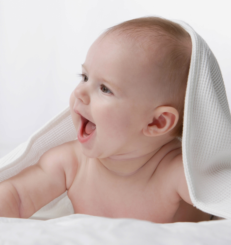 Smiling baby underneath white and blue blanket as a visual representation of Baby Powder Fragrance Oil available at Village Craft and Candle || Bébé souriant sous une couverture blanche et bleue comme représentation visuelle de l'huile parfumée en poudre pour bébé disponible chez Village Craft and Candle