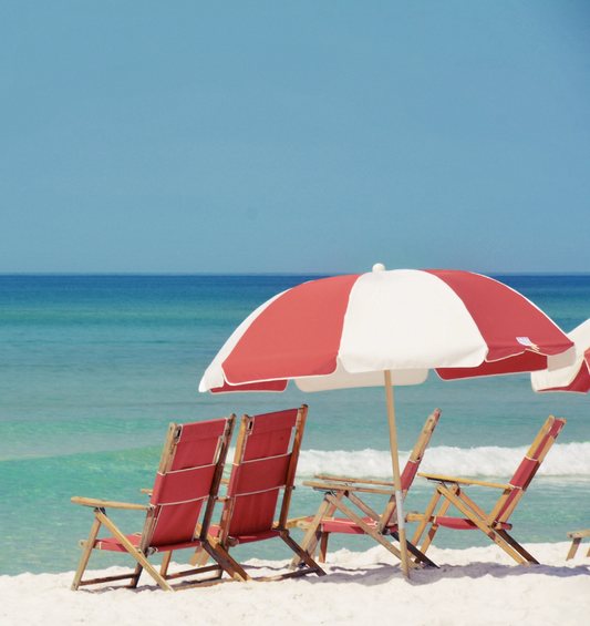  Chaises de plage et parasols avec l'océan bleu et une plage de sable comme représentation visuelle de l'huile parfumée Journée à la Plage chez Village Craft and Candle.