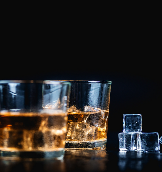 Glass of bourbon with ice cubes in the dark as a visual representation of Bourbon Fragrance Oil available at Village Craft and Candle 