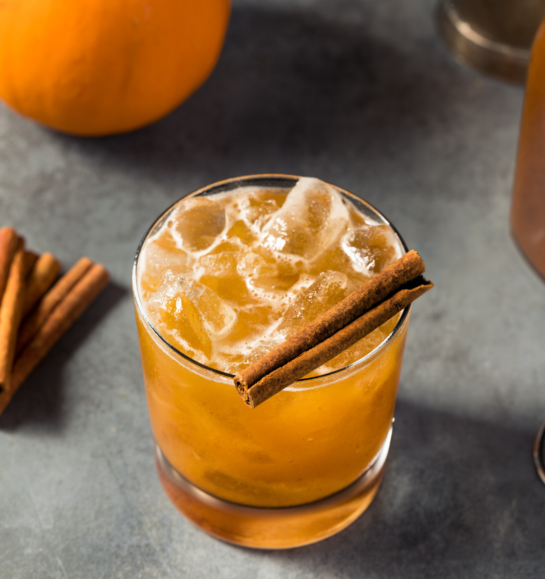 Pumpkin bourbon cocktail with crushed ice and cinnamon sticks on counter as a visual representation of Bourbon Pumpkin Fragrance Oil available at Village Craft and Candle || Cocktail à la citrouille et au bourbon avec de la glace pilée et des bâtons de cannelle sur le comptoir comme représentation visuelle de l'Huile parfumée Citrouille Bourbon disponible chez Village Craft & Candle.