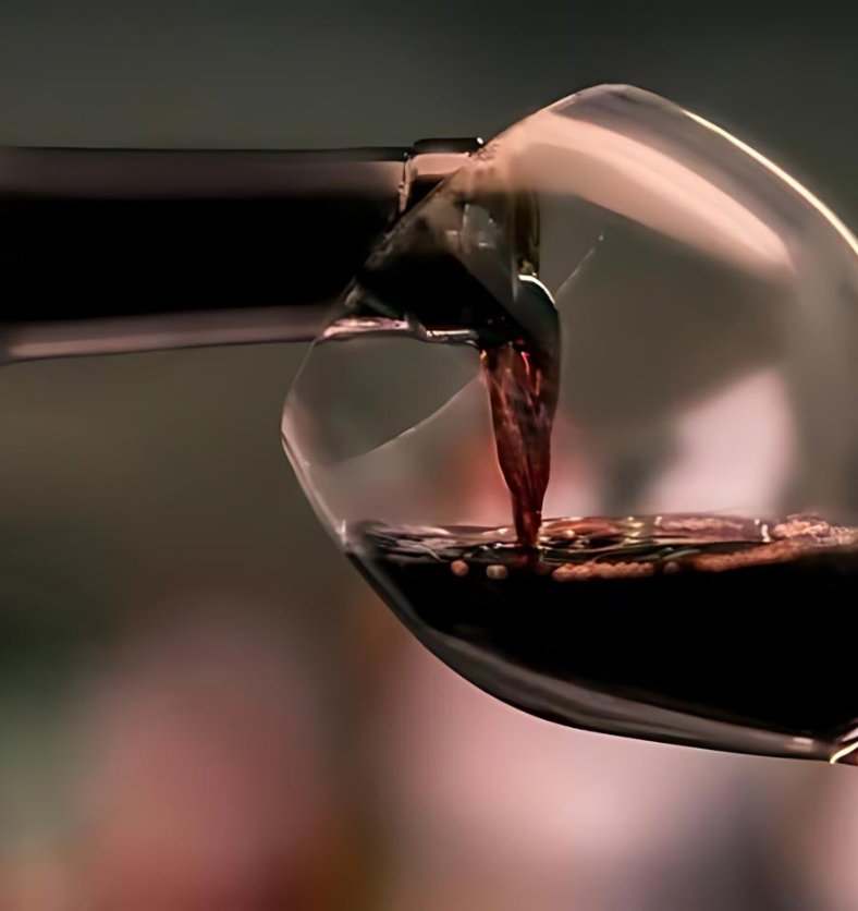 Close up of red wine being poured into a wine glass as a visual representation of Cabernet Fragrance Oil available at Village Craft and Candle || Gros plan de vin rouge versé dans un verre à vin comme représentation visuelle de l'huile parfumée Cabernet disponible chez Village Craft and Candle