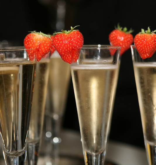 Campange flutes with strawberries on the lips of the glasses as a visual representation of Strawberries and Champagne Fragrance Oil available at Village Craft and Candle 