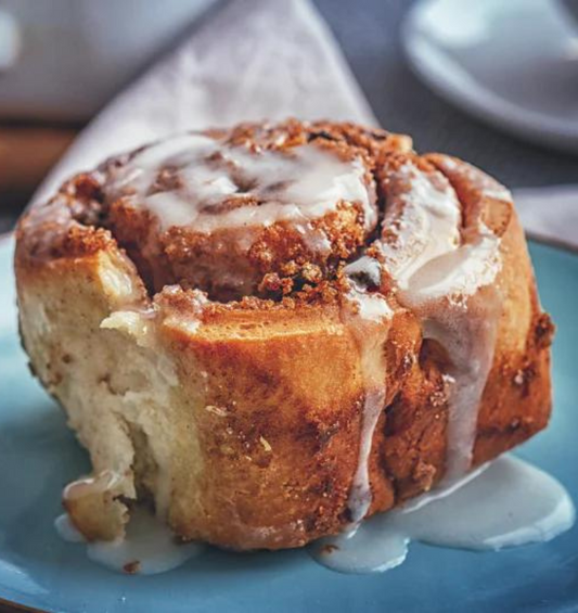  Petit pain à la cannelle arrosé de glaçage sur une assiette bleue comme représentation visuelle de l'huile parfumée Cinnabonne disponible chez Village Craft and Candle