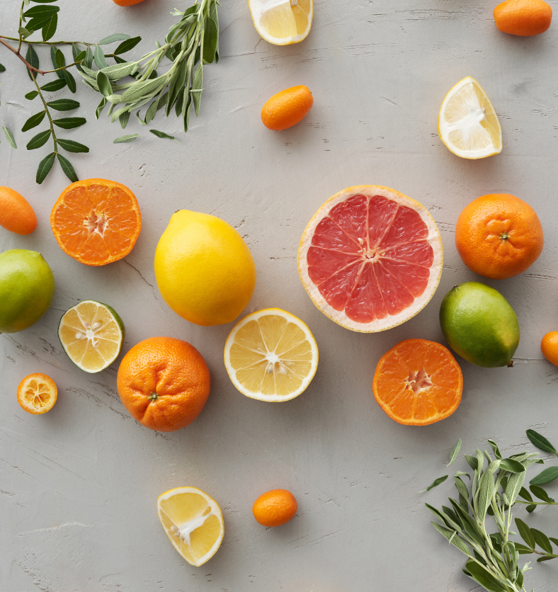 Cut citrus fruits on white table as a visual representation of Citrus & Sage Fragrance Oil available at Village Craft and Candle || Coupez les agrumes sur une table blanche comme représentation visuelle de l'huile parfumée d'agrumes et de sauge disponible chez Village Craft and Candle.