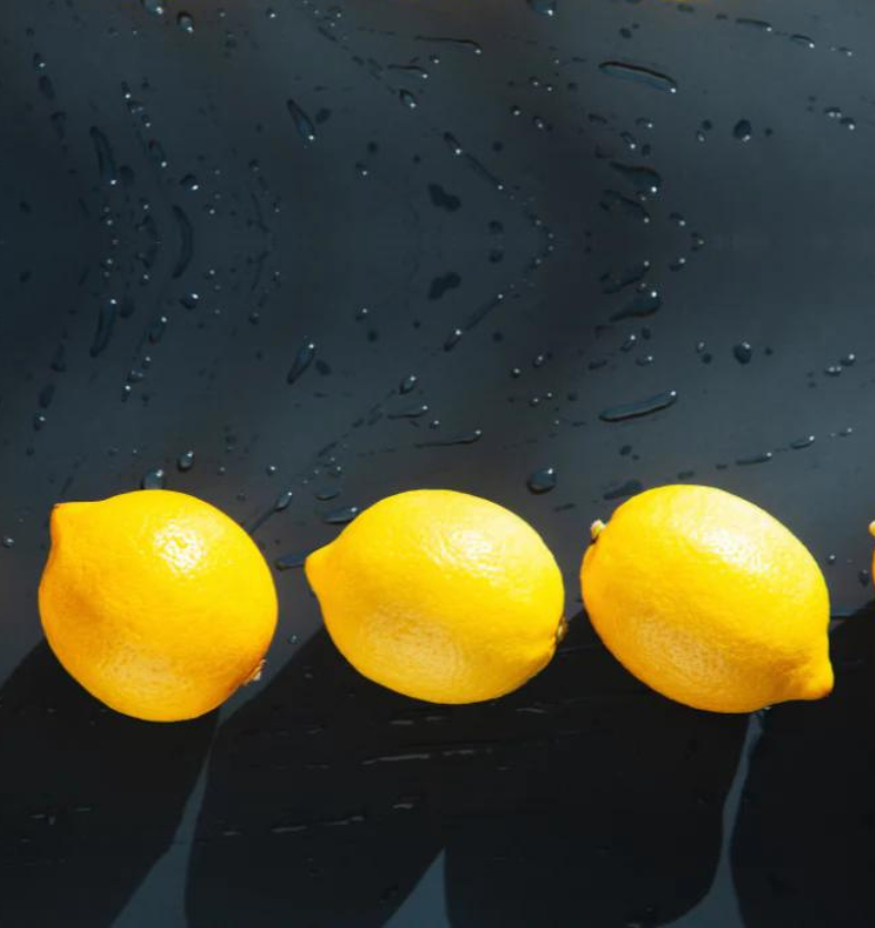 Four lemons on a wet black table as a visual representation of Clean Lemon Fragrance Oil available at Village Craft and Candle || Quatre citrons sur une table noire humide comme représentation visuelle de l'huile parfumée au citron propre disponible chez Village Craft and Candle