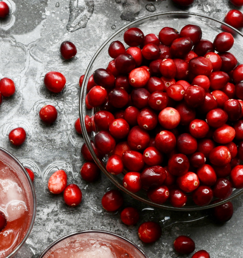 Glass bowl of cranberries on grey countertop as a visual representation of Cranberry Fragrance Oil available at Village Craft and Candle || Bol en bois de canneberges posé sur une table en bouleau comme représentation visuelle de l'huile parfumée de canneberge disponible chez Village Craft and Candle