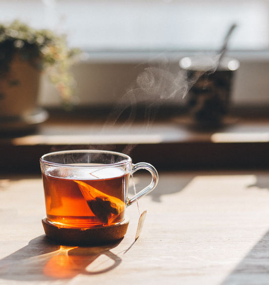  Verre fumant de thé gris précoce au soleil avec des plantes en pot en arrière-plan comme représentation visuelle de l'huile parfumée de thé Earl Grey disponible chez Village Craft and Candle