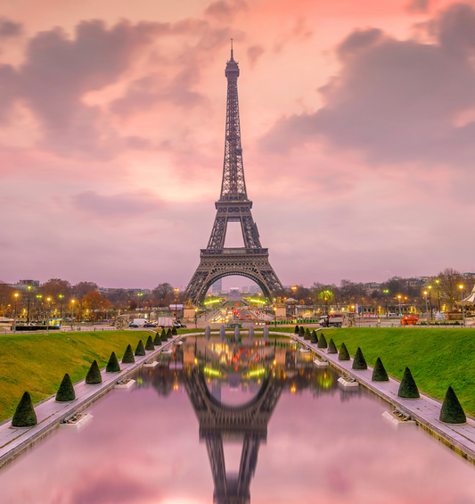  Vue de la Tour Eiffel avec un ciel rose et son reflet dans l'eau comme représentation visuelle de l'huile parfumée Evening Mischief disponible chez Village Craft and Candle.