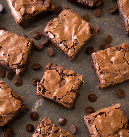  Carrés de brownie entourés de pépites de chocolat comme représentation visuelle de l'huile parfumée Hot Fudge Brownie disponible chez Village Craft and Candle.