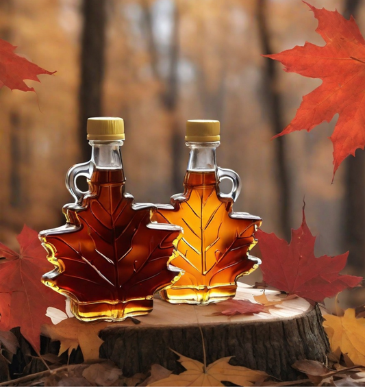 Two bottle of maple syrup in maple leaf shaped bottles on tree stump surrounded by red maple leaves as a visual representation of Maple Syrup Fragrance Oil available at Village Craft and Candle 