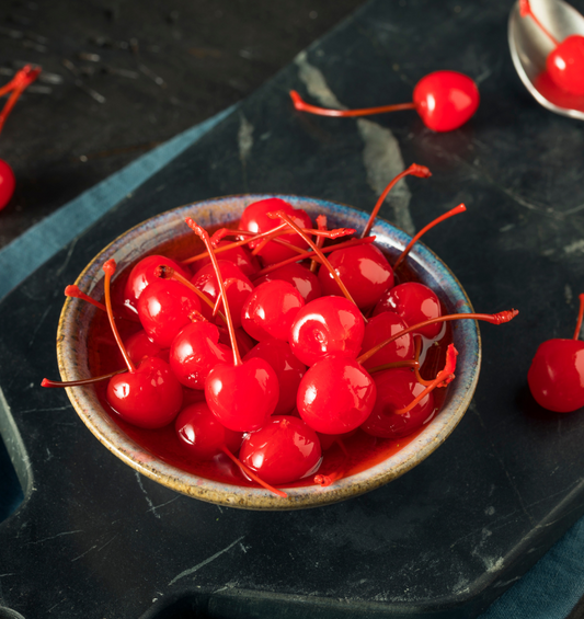  Un bol de cerises au marasquin sur une planche à découper en marbre noir comme représentation visuelle de l'huile parfumée de cerise au marasquin disponible chez Village Craft and Candle