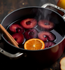 Mulled Plum Fragrance Oil represented by simmering plums with orange slices and cinnamon sticks, capturing a warm, fruity, spiced aroma || Huile parfumée Mulled Plum représentée par des prunes mijotées avec des tranches d’orange et des bâtons de cannelle, évoquant un arôme chaud, fruité et épicé.