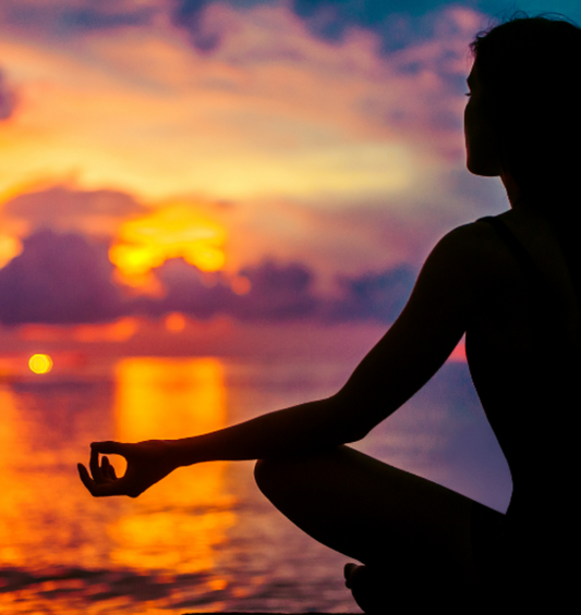 Woman meditating in front of an ocean sunset as a visual representation of Namaste Fragrance Oil available at Village Craft and Candle 